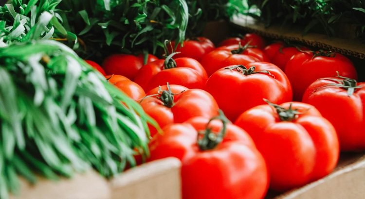 Vibrant red tomatoes and fresh greens displayed at a London farmer's market, showcasing organic produce.